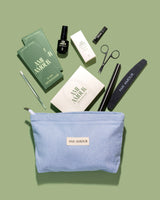 Mani starter kit flat lay — blue Ami Amour pouch with scissors, buffer and manicure tools on sage green.